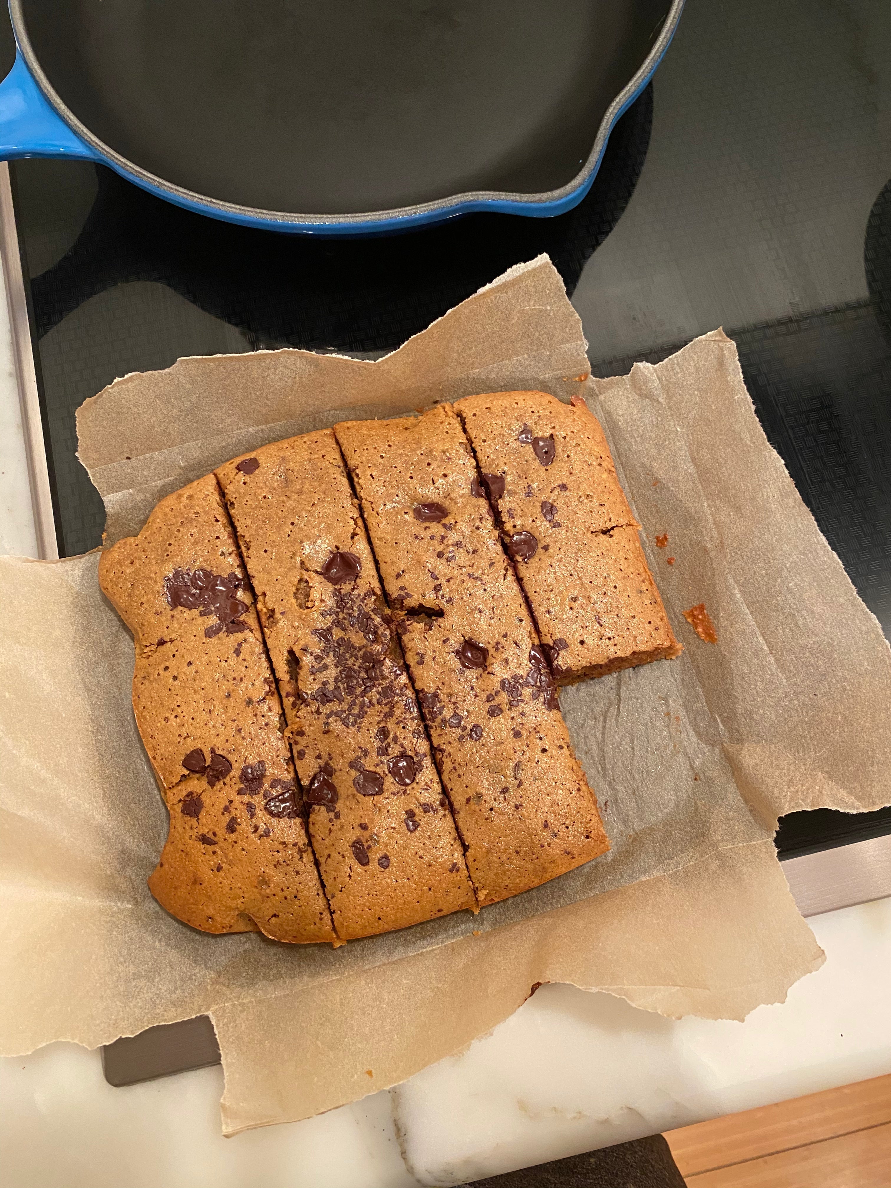 Dairy-free, gluten-free coffee cake cut into thick bars with golden edges and melted chocolate chips, served on parchment paper with a cup of black coffee nearby.