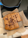 Dairy-free, gluten-free coffee cake cut into thick bars with golden edges and melted chocolate chips, served on parchment paper with a cup of black coffee nearby.